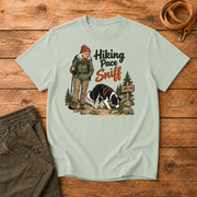 Adventure Dogs Life T-shirt in bay, a muted light green, featuring a hiker and border collie on a mountain trail with "Hiking Pace Sniff" lettering.